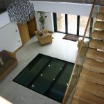 Floating staircase and glass floor section sat on a steel frame looking into basement swimming pool area.